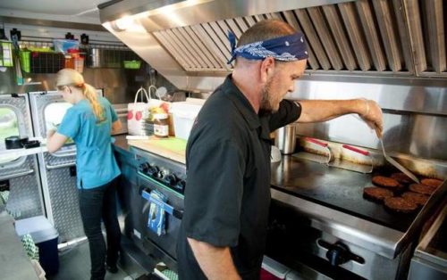 Kenny Richards cooks black bean burgers on the grill as Amber Davis cuts strawberries inside the Emergency Munchie Truck at the Sagamore West Farmers Market in West Lafayette. / Brent Drinkut/Journal & Courier